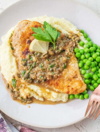 Chicken piccata served with mashed potatoes and peas on a plate.