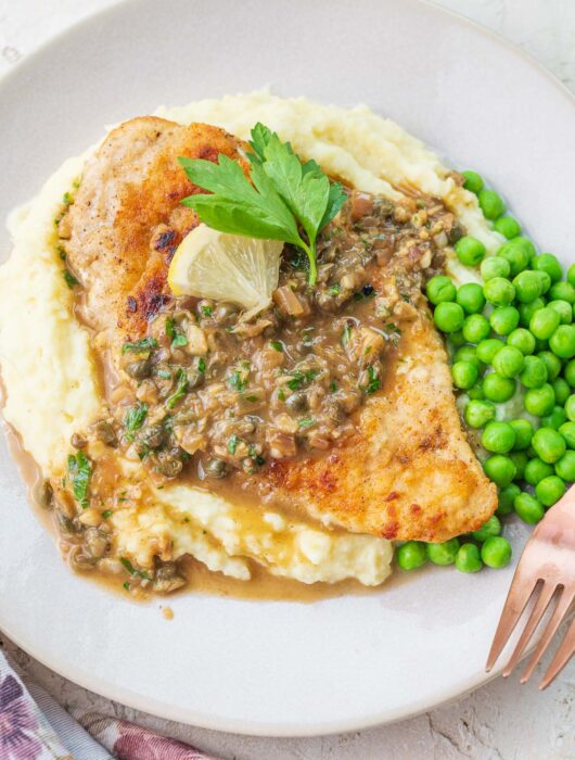 Chicken piccata served with mashed potatoes and peas on a plate.