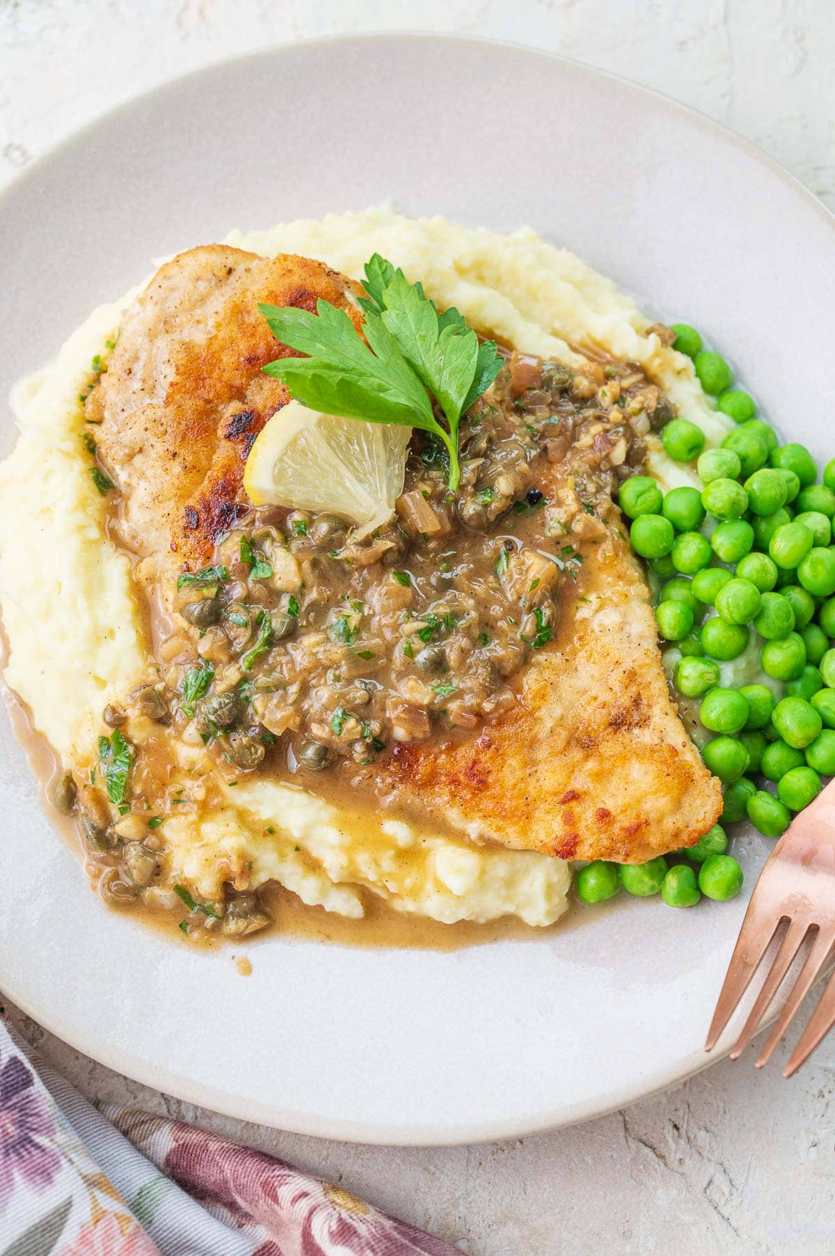 Chicken piccata with mashed potatoes and peas on a plate.