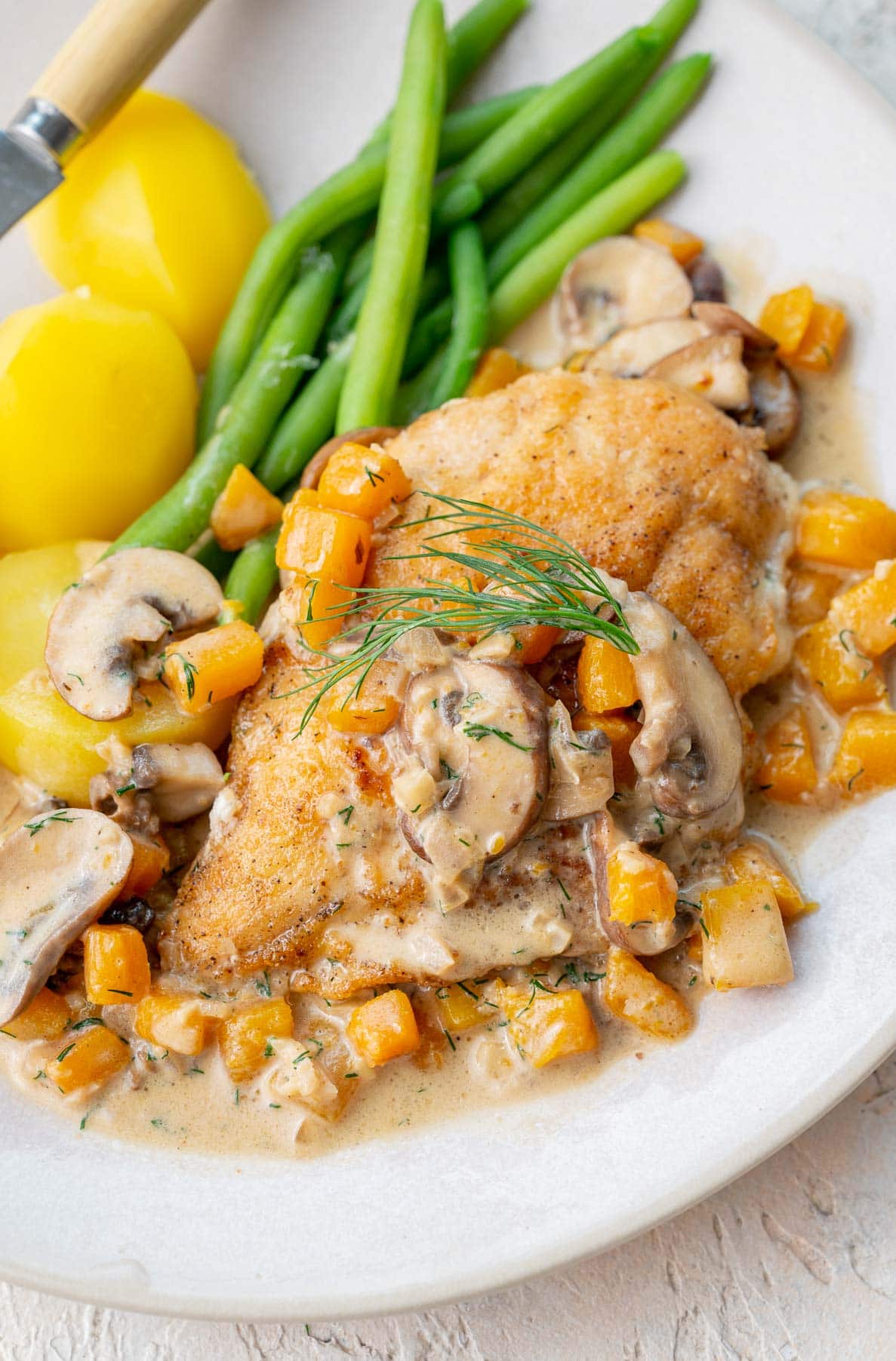 Chicken with Creamy Butternut Squash and Mushroom Sauce on a beige plate served with green beans and potatoes.