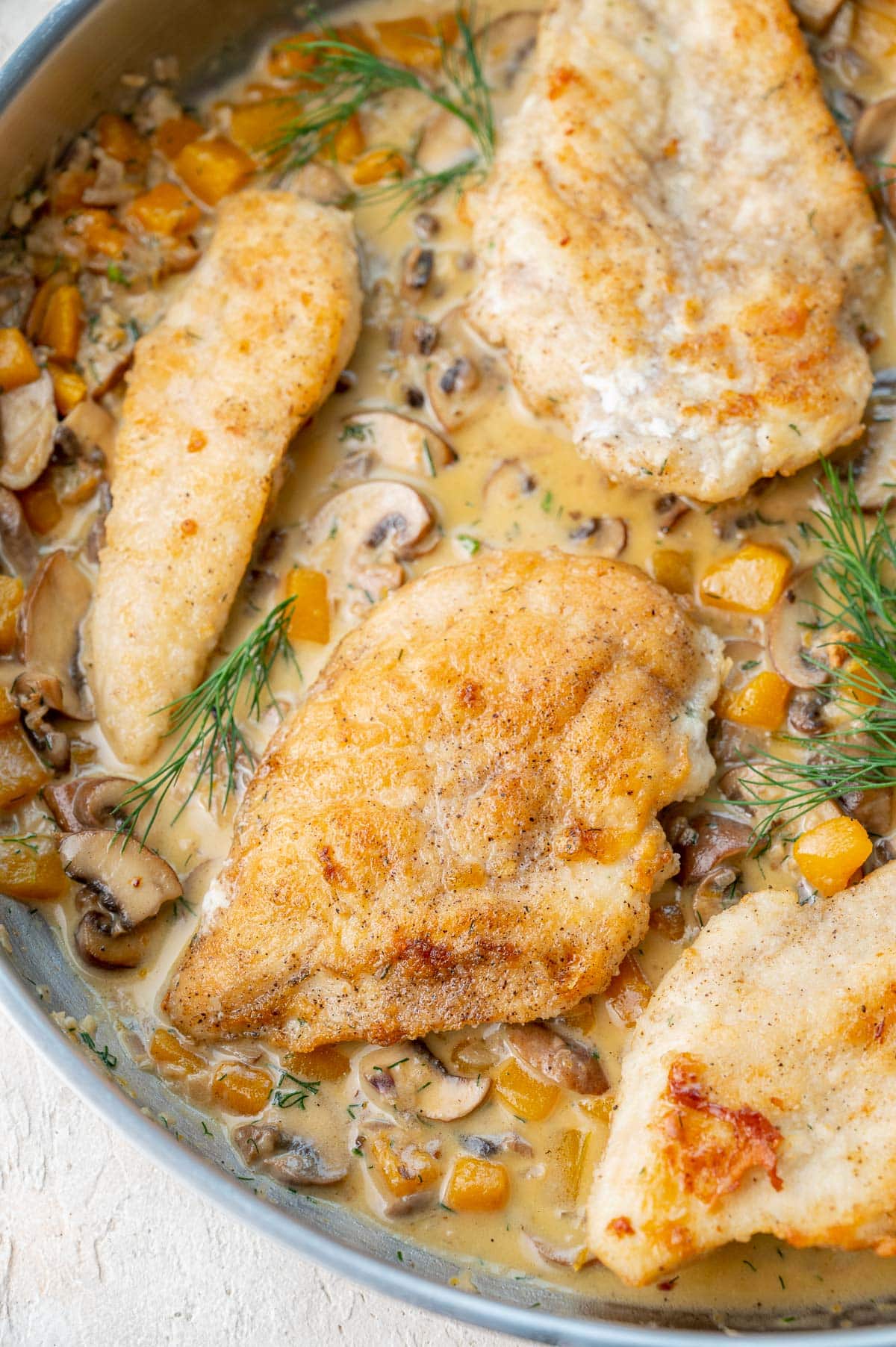 A close up photo of chicken with Creamy Butternut Squash and Mushroom Sauce in a pan.