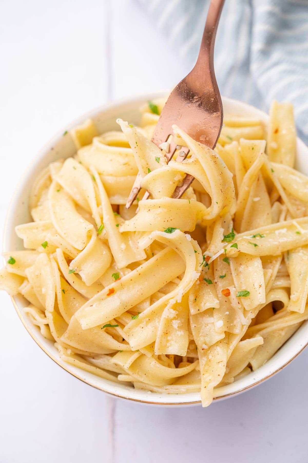 Garlic butter noodles in a white bowl stuck on a fork.