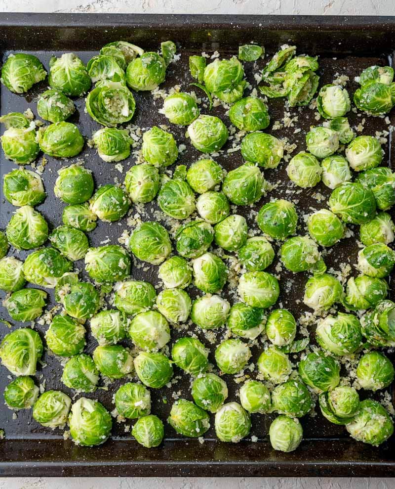 Brussels sprouts ready to be baked on a black baking sheet.