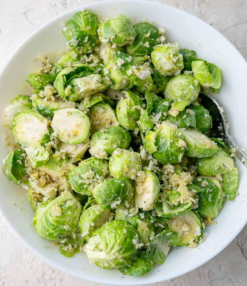 Brussel sprouts tossed with cheese, breadcrumbs, and spices in a white bowl.