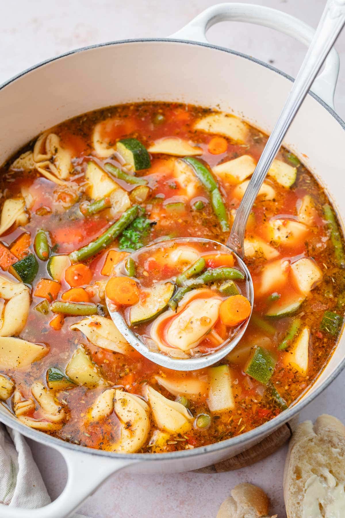 Vegetable tortellini soup in a white pot and on a ladle.