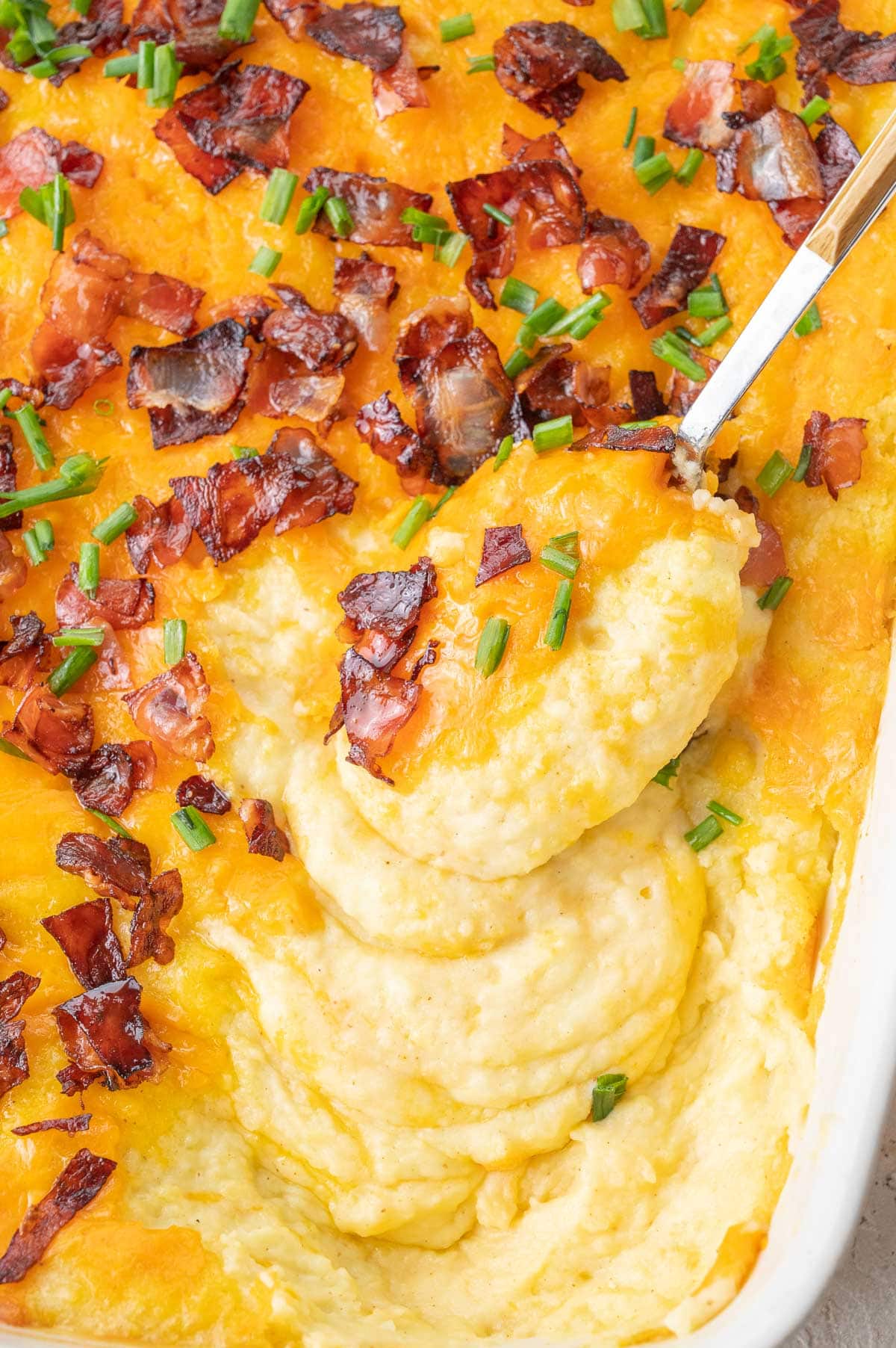 A close up photo of loaded mashed potato casserole in a white baking dish.