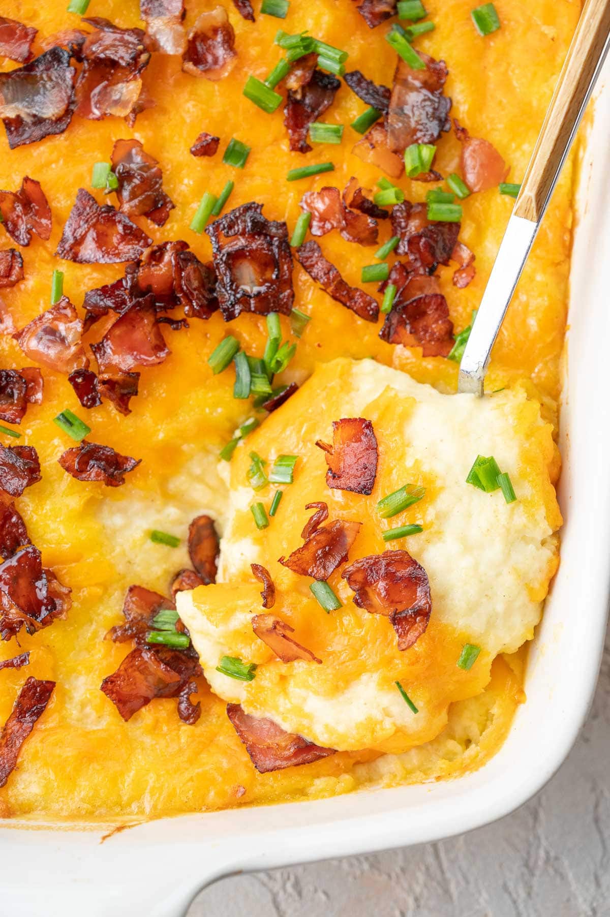 A close up photo of loaded mashed potato casserole in a baking dish and on a spoon.