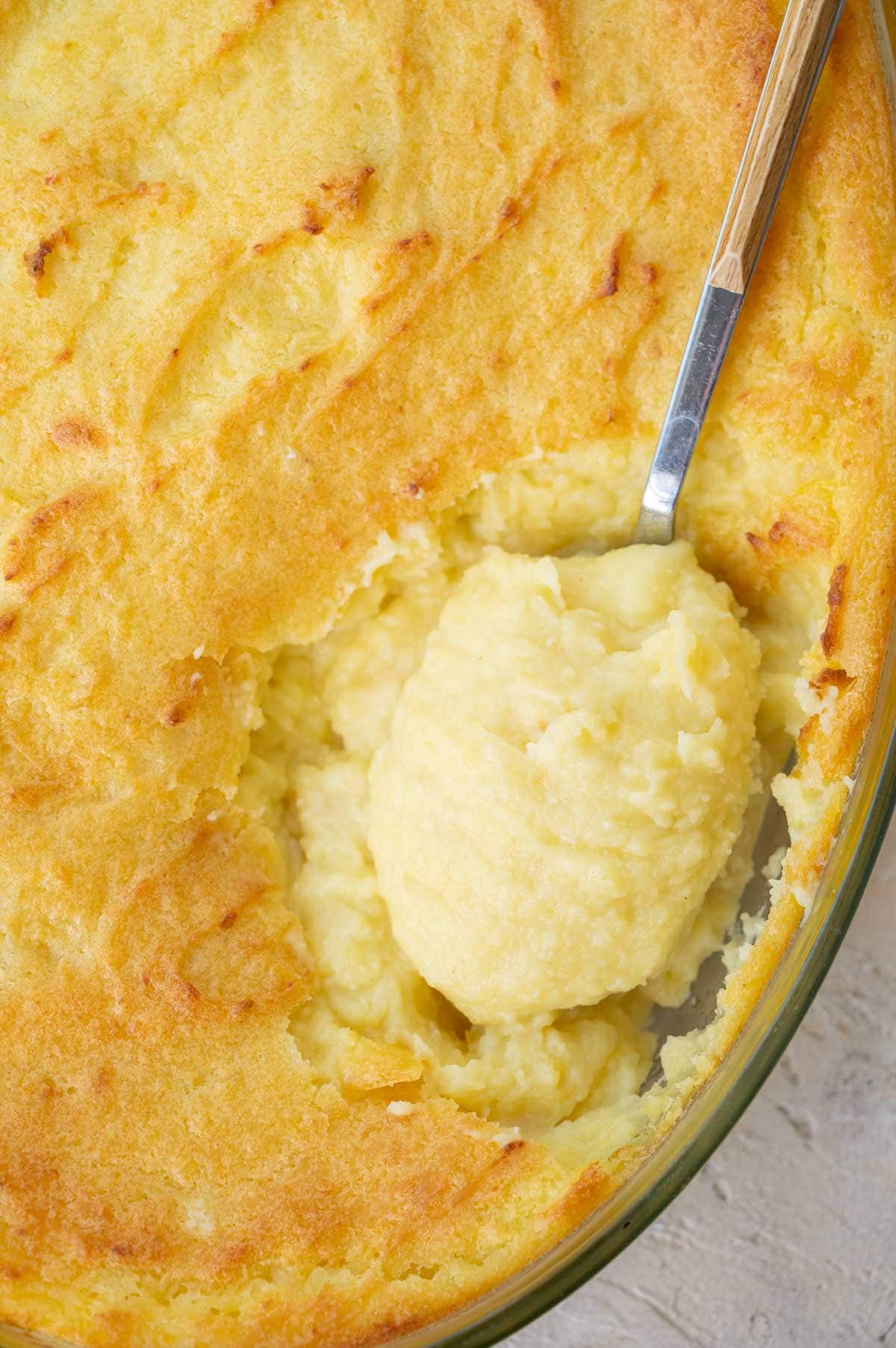 Make-ahead mashed potatoes are being scooped with a large spoon from a baking dish.