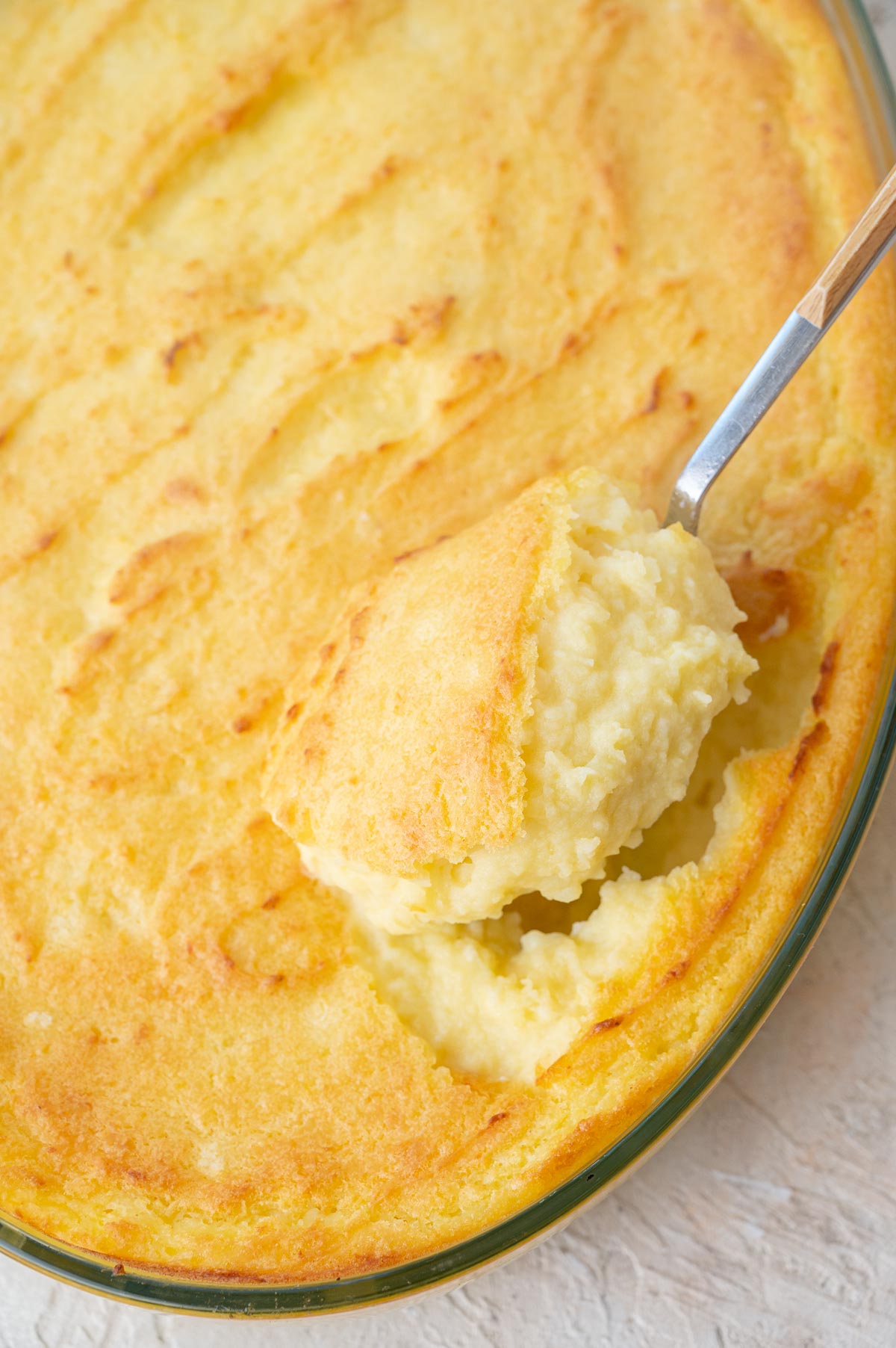 Make-ahead mashed potatoes are being scooped with a large spoon from a baking dish.