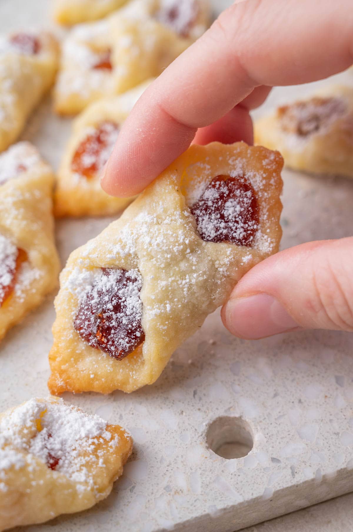 Jam-filled cookie held in hand on a grey background.