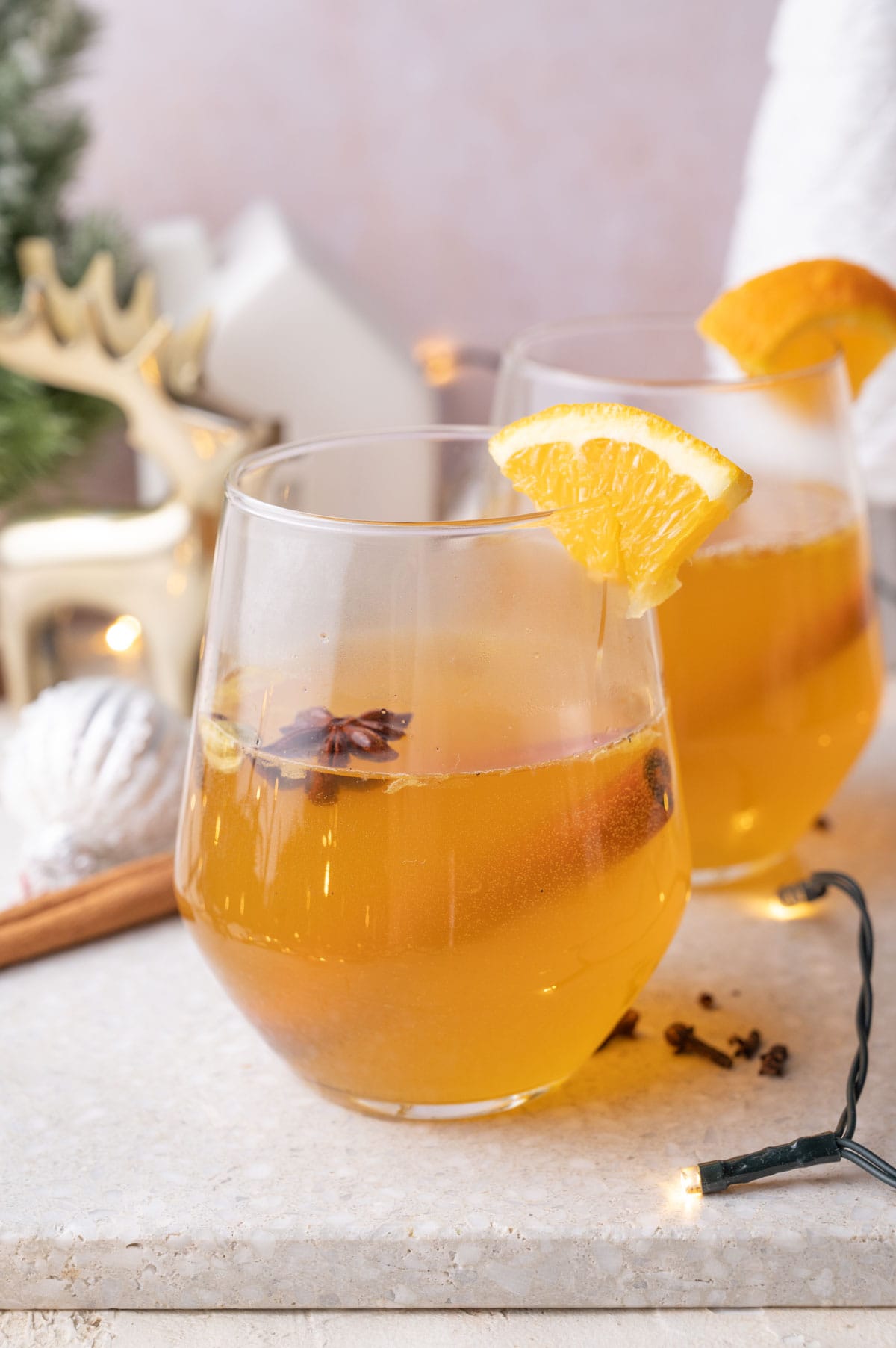 Two glassed with mulled white wine on a grey stone board. Christmas decoration in the background.