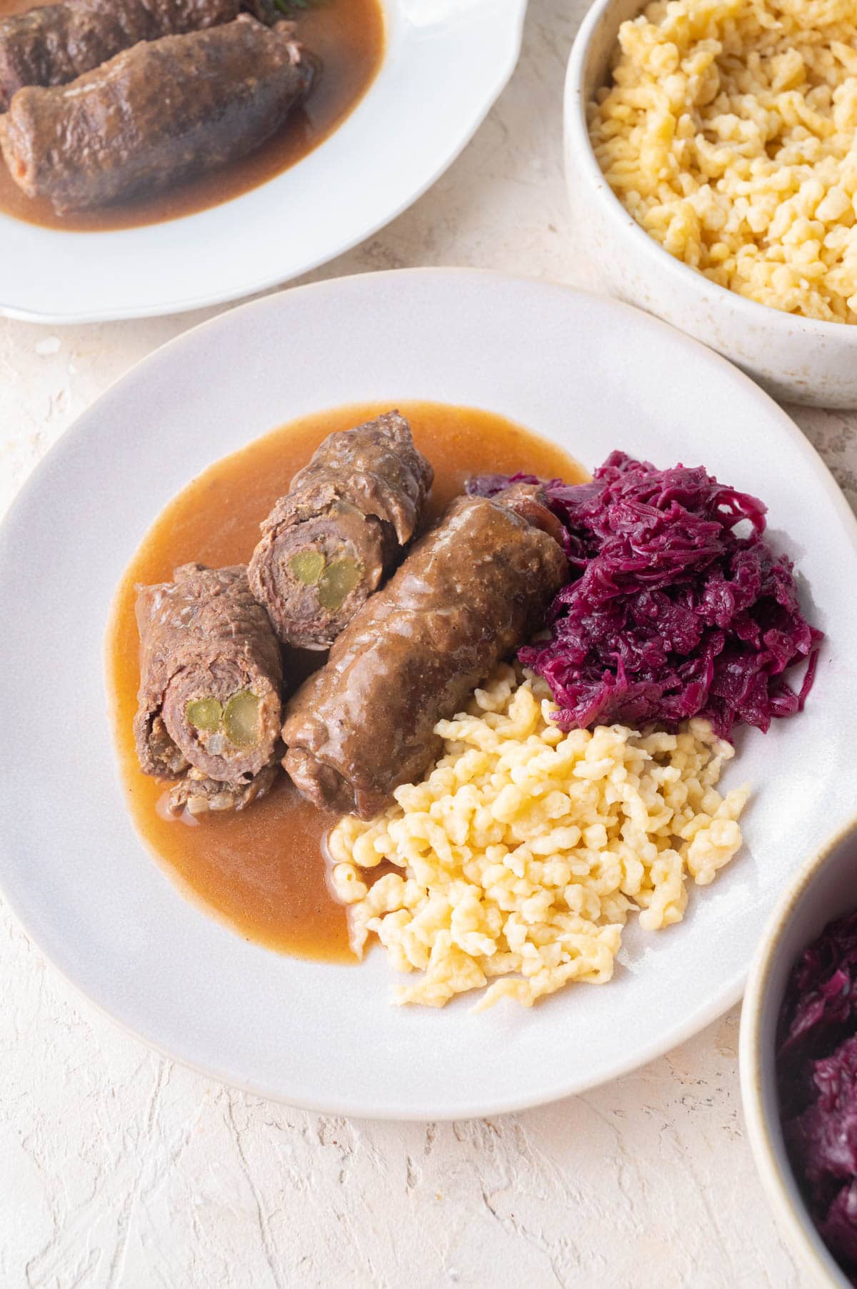Rouladen with gravy, braised red cabbage, and Spätzle on a beige plate.