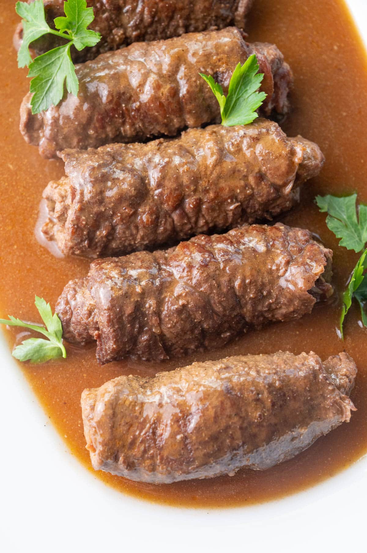 Rouladen with gravy on a white plate, sprinkled with parsley.