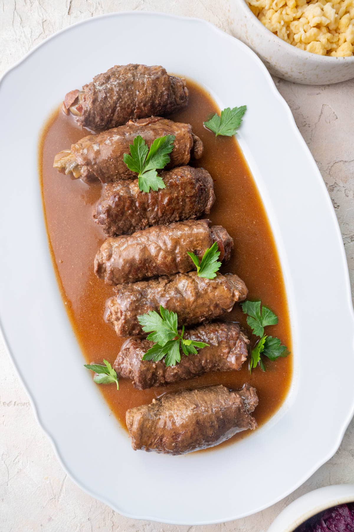 Overhead photo of Rouladen in dark gravy on a white plate.