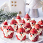 Santa strawberries on a white plate. Christmas decorations in the background.