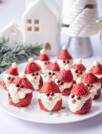 Santa strawberries on a white plate. Christmas decorations in the background.