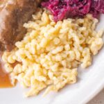 Spätzle served with Rouladen and braised red cabbage on a plate.