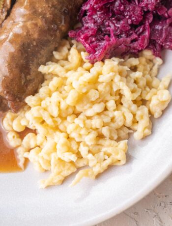 Spätzle served with Rouladen and braised red cabbage on a plate.