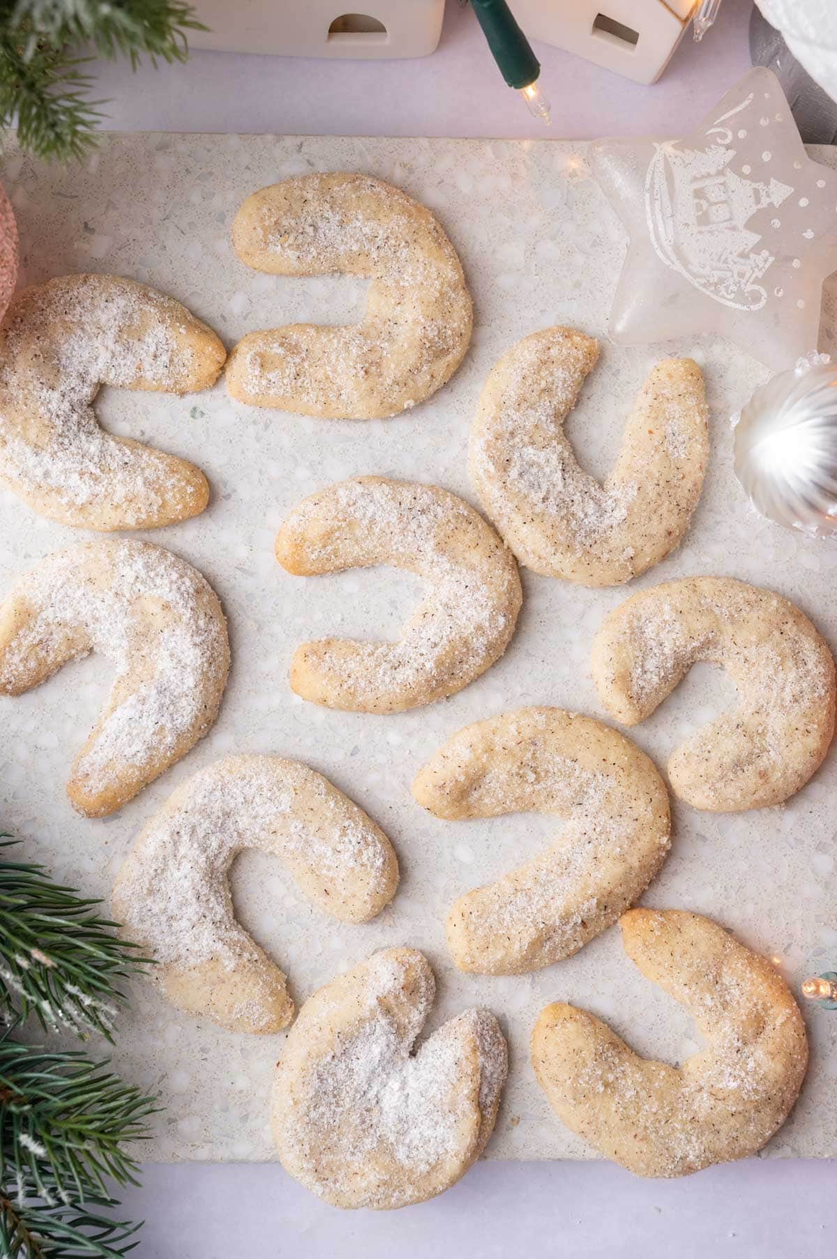 Vanillekipferl on a stone board surrounded by Christmas decorations.