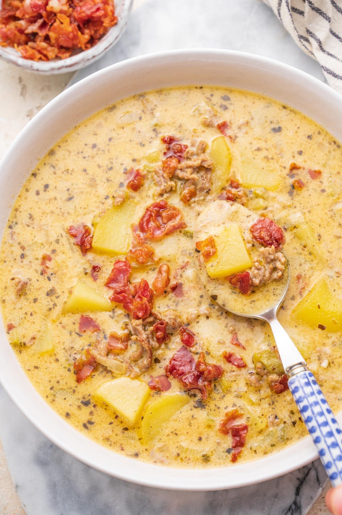 Cheeseburger chowder soup in a white bowl. Blue spoon on the side.