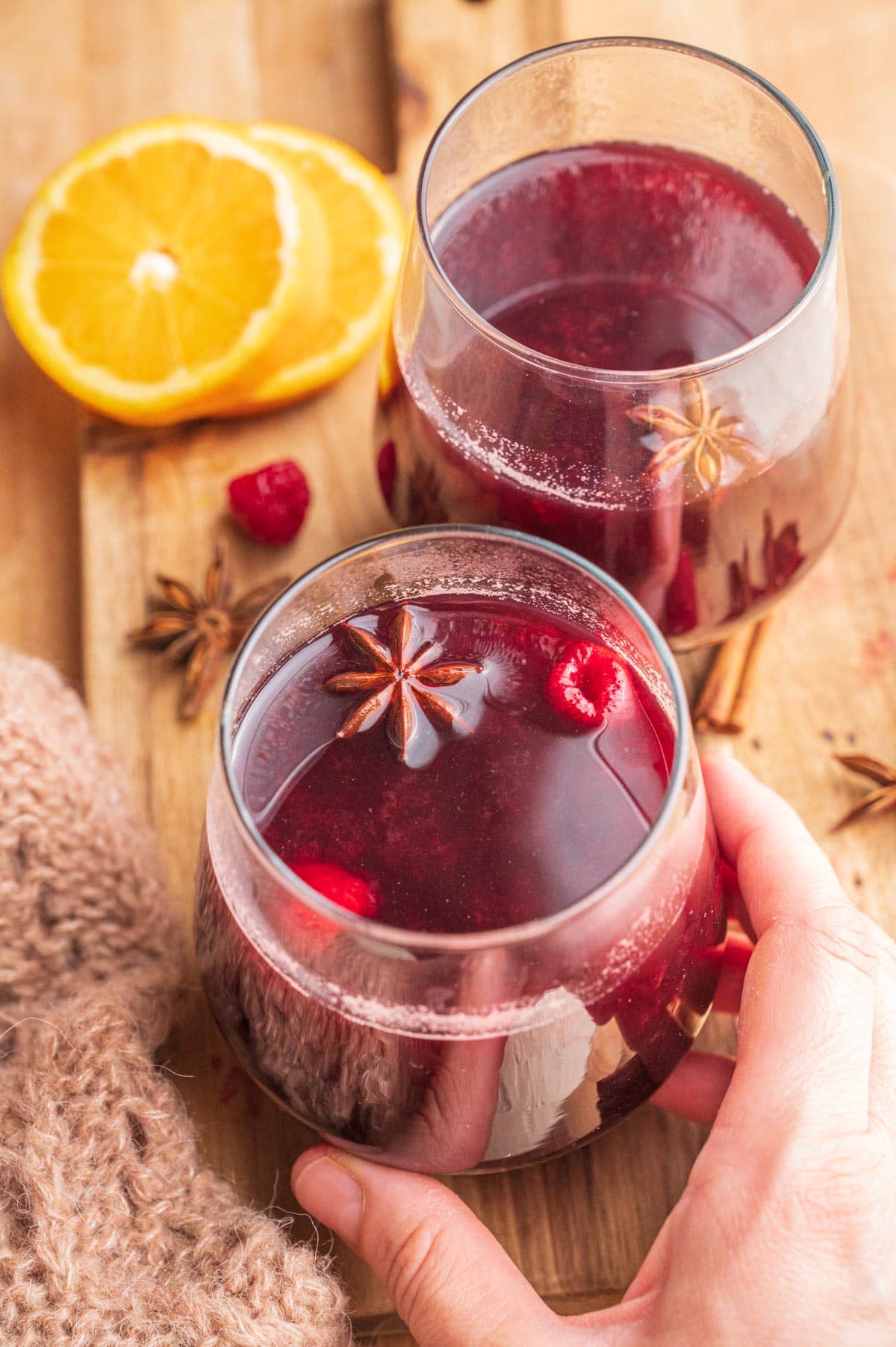 Two glassed with Polish mulled wine on a wooden board. One glass is being held by a hand.