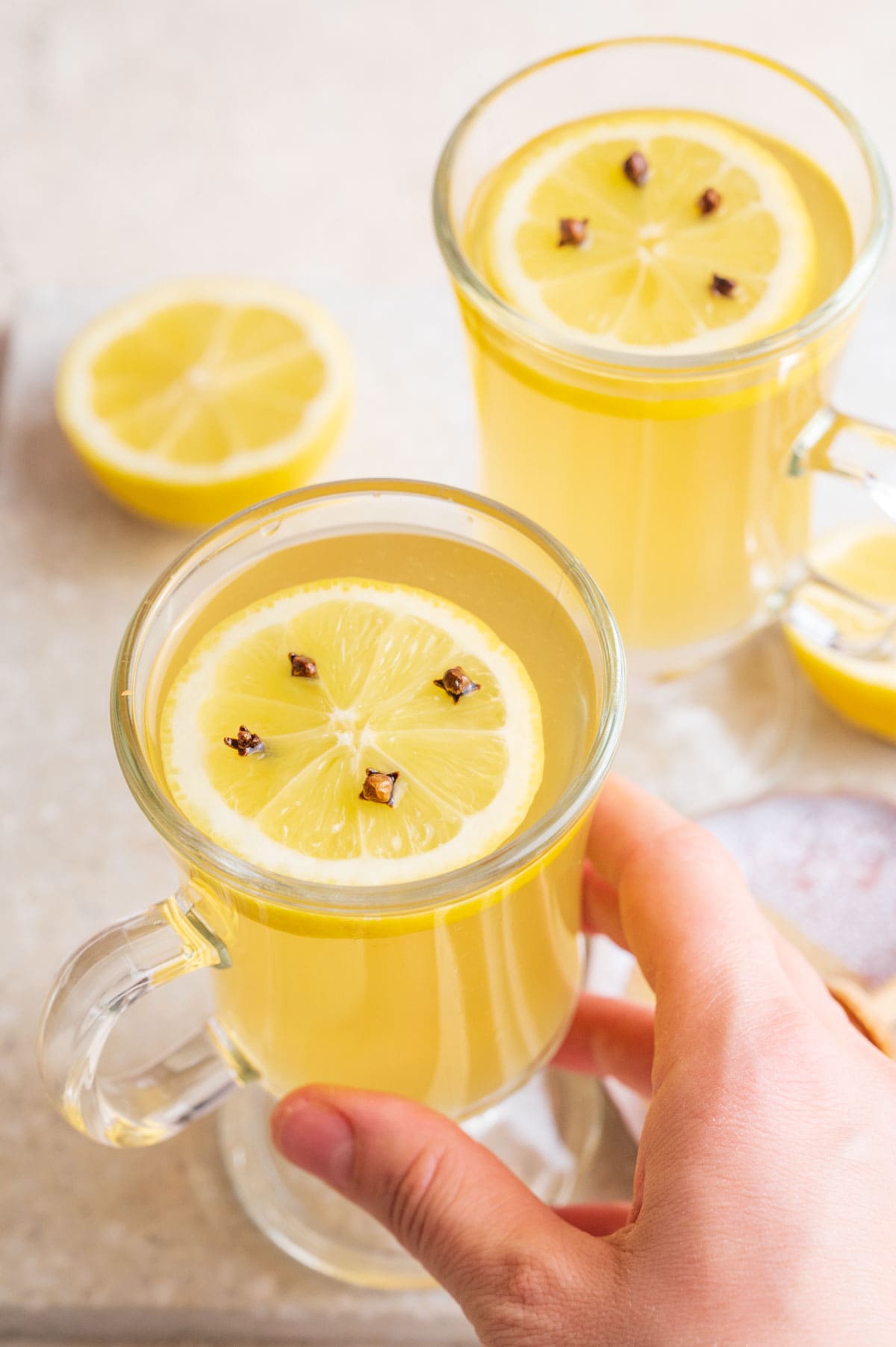 Two glasses with hot toddy. Lemons and honey in the background. One glass is held in a hand.