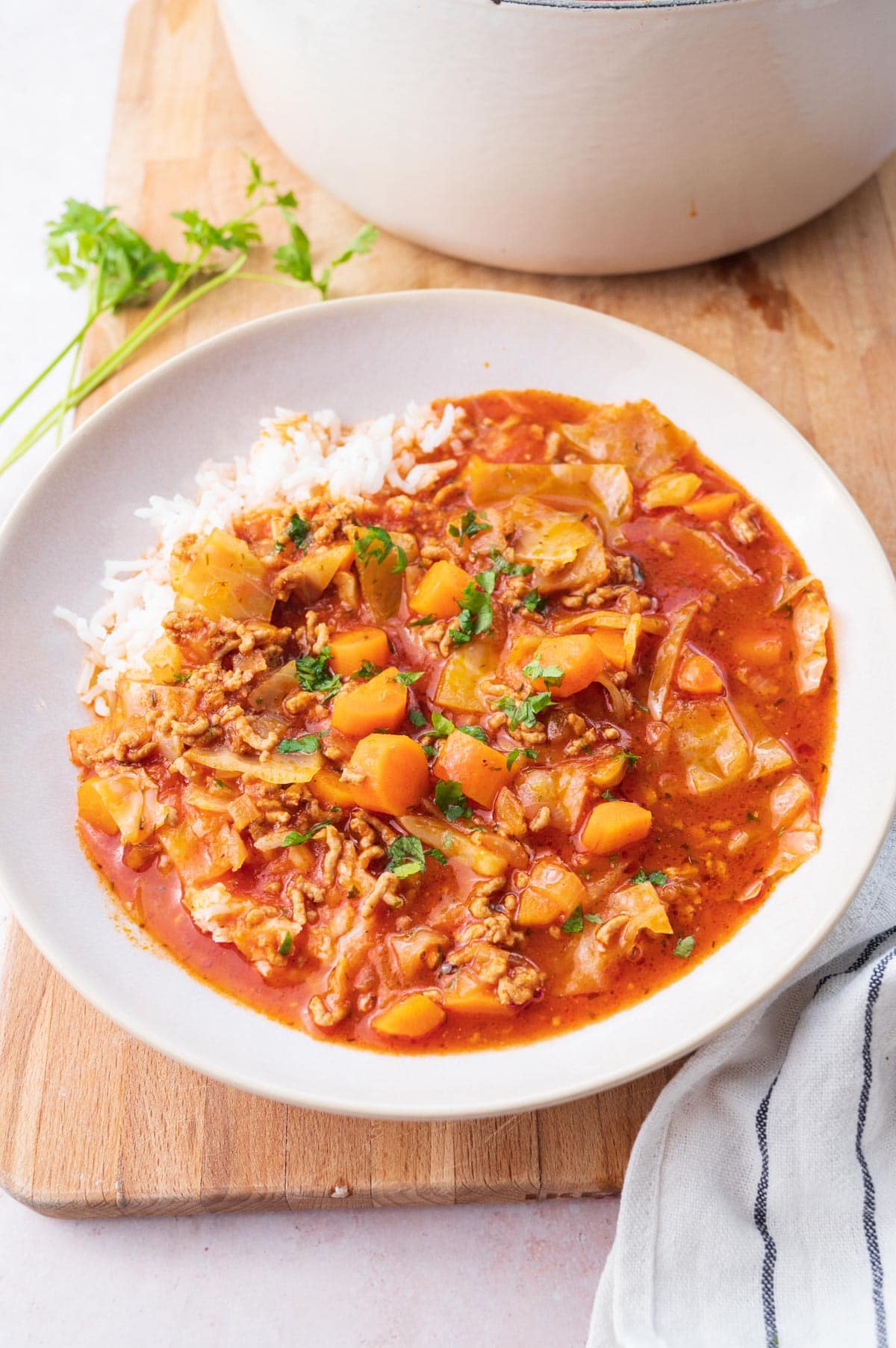 Cabbage roll soup served with rice in a beige bowl on a wooden board.