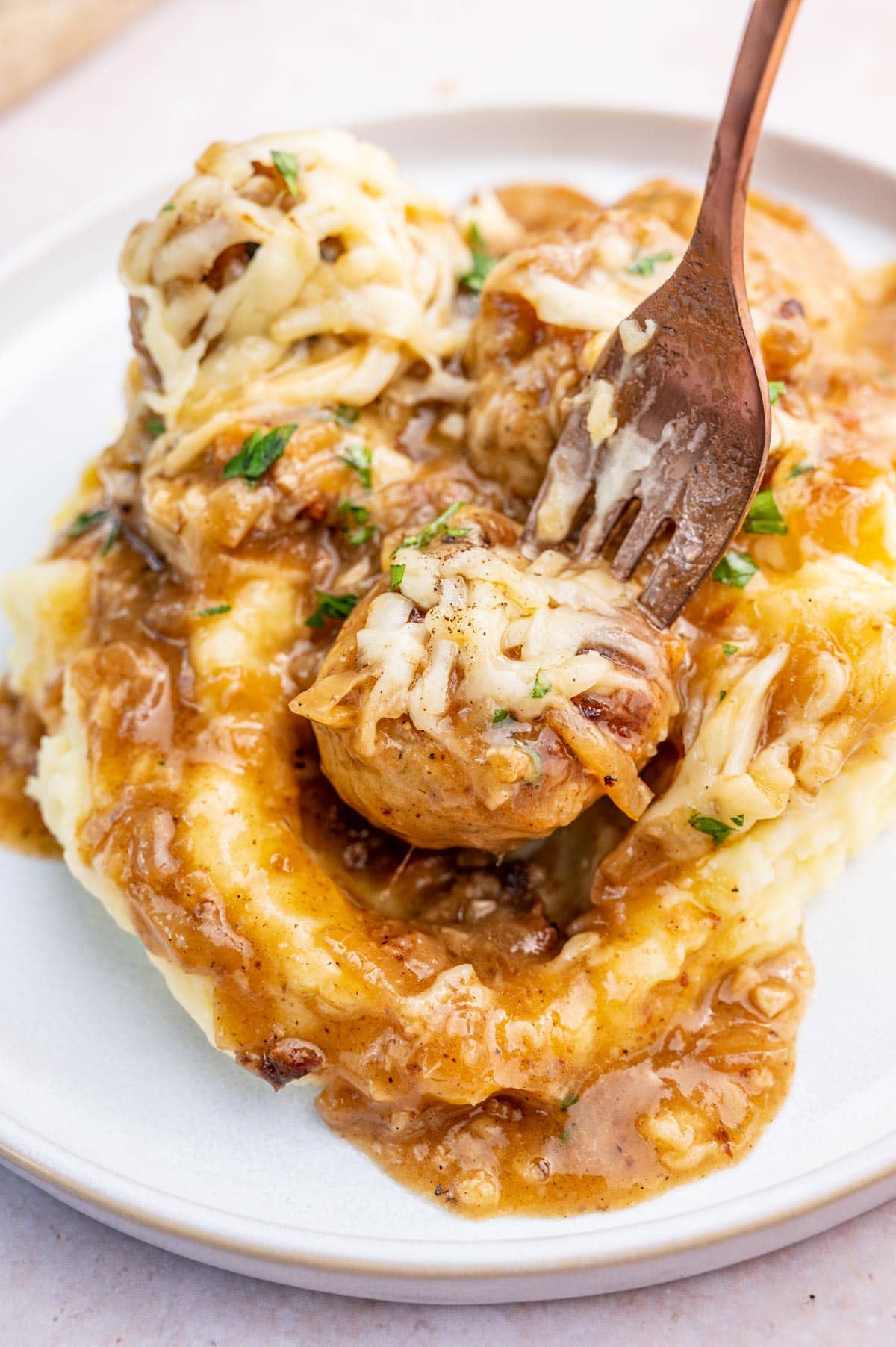 French onion meatballs with gravy and mashed potatoes on a white plate.