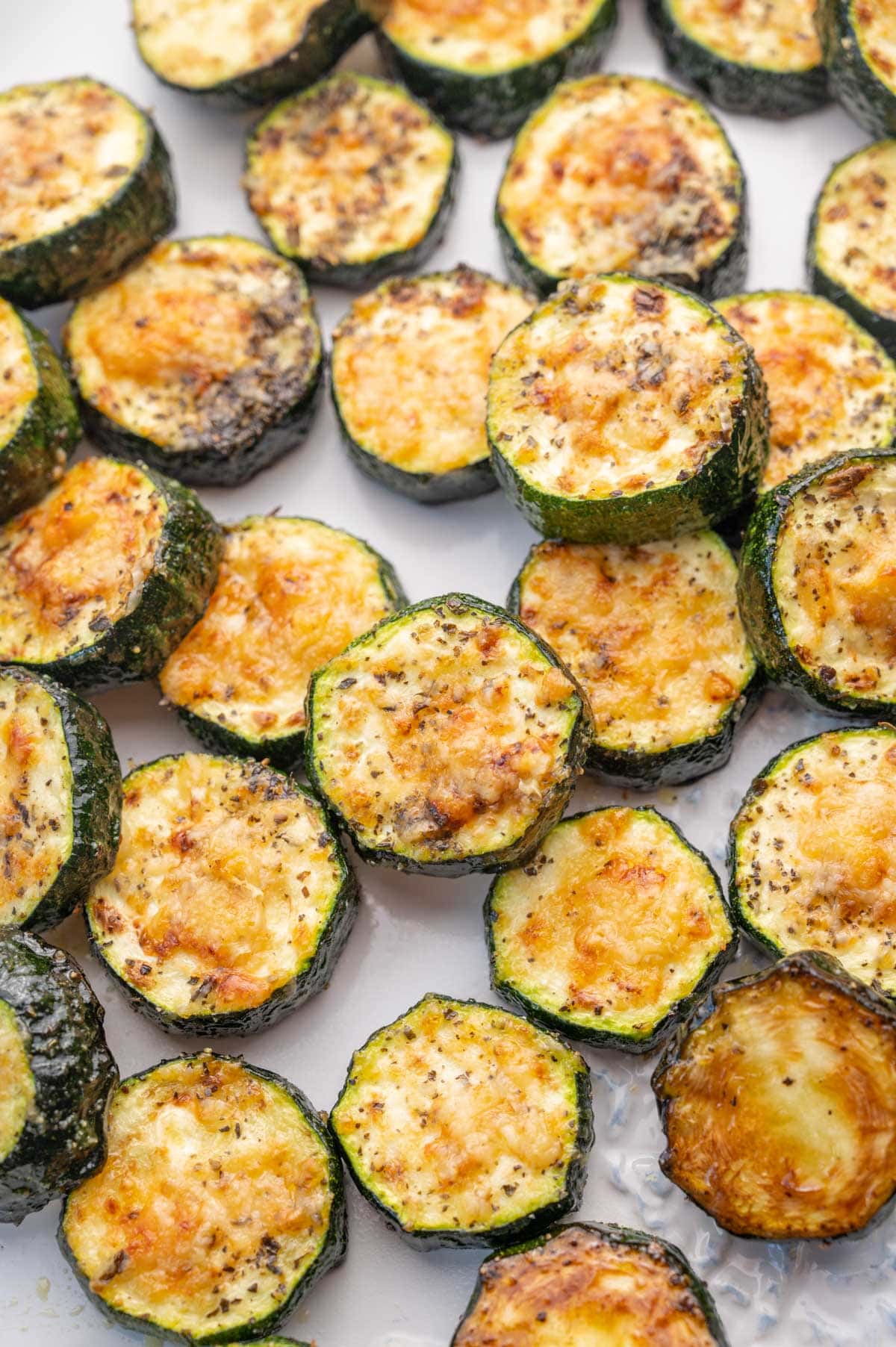 A close up photo of baked parmesan zucchini on a white plate.