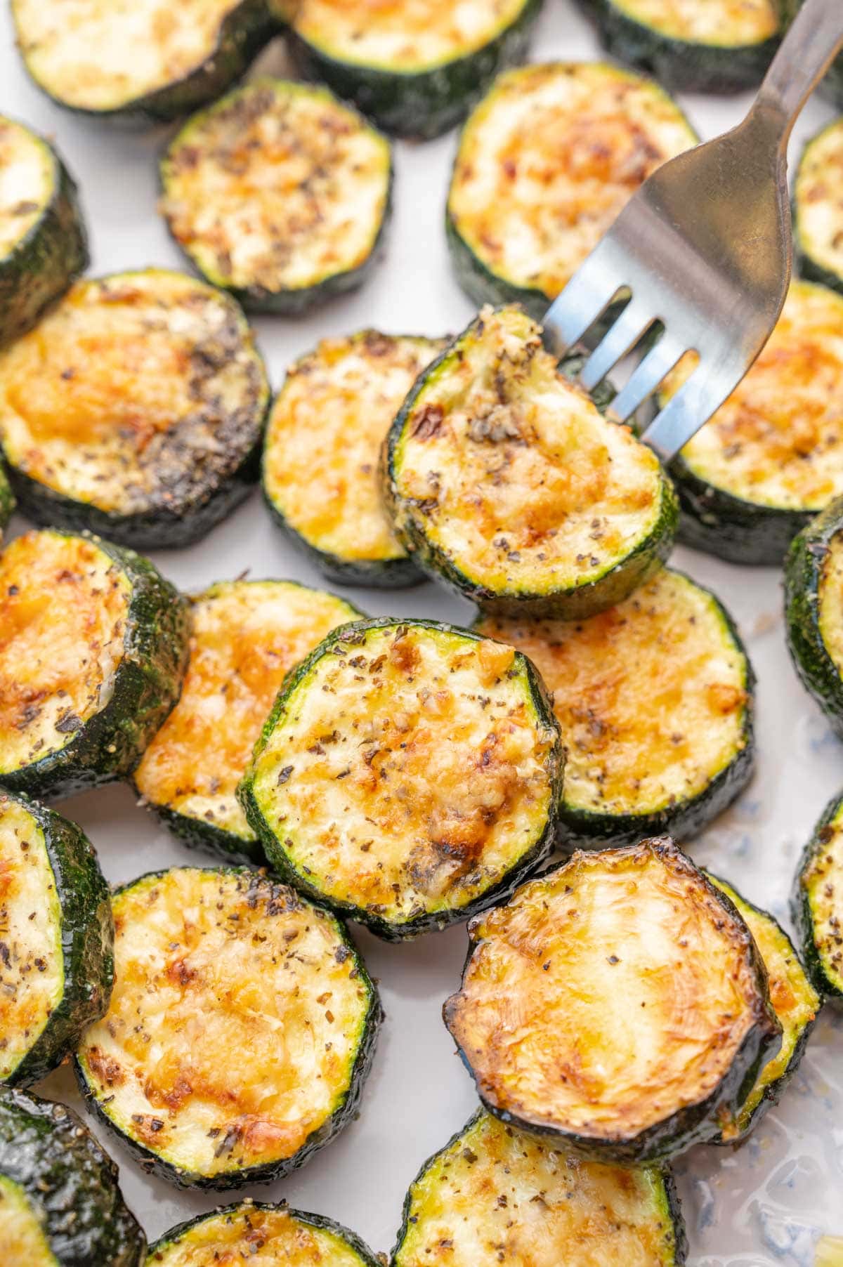 A close up photo of baked parmesan zucchini on a white plate.