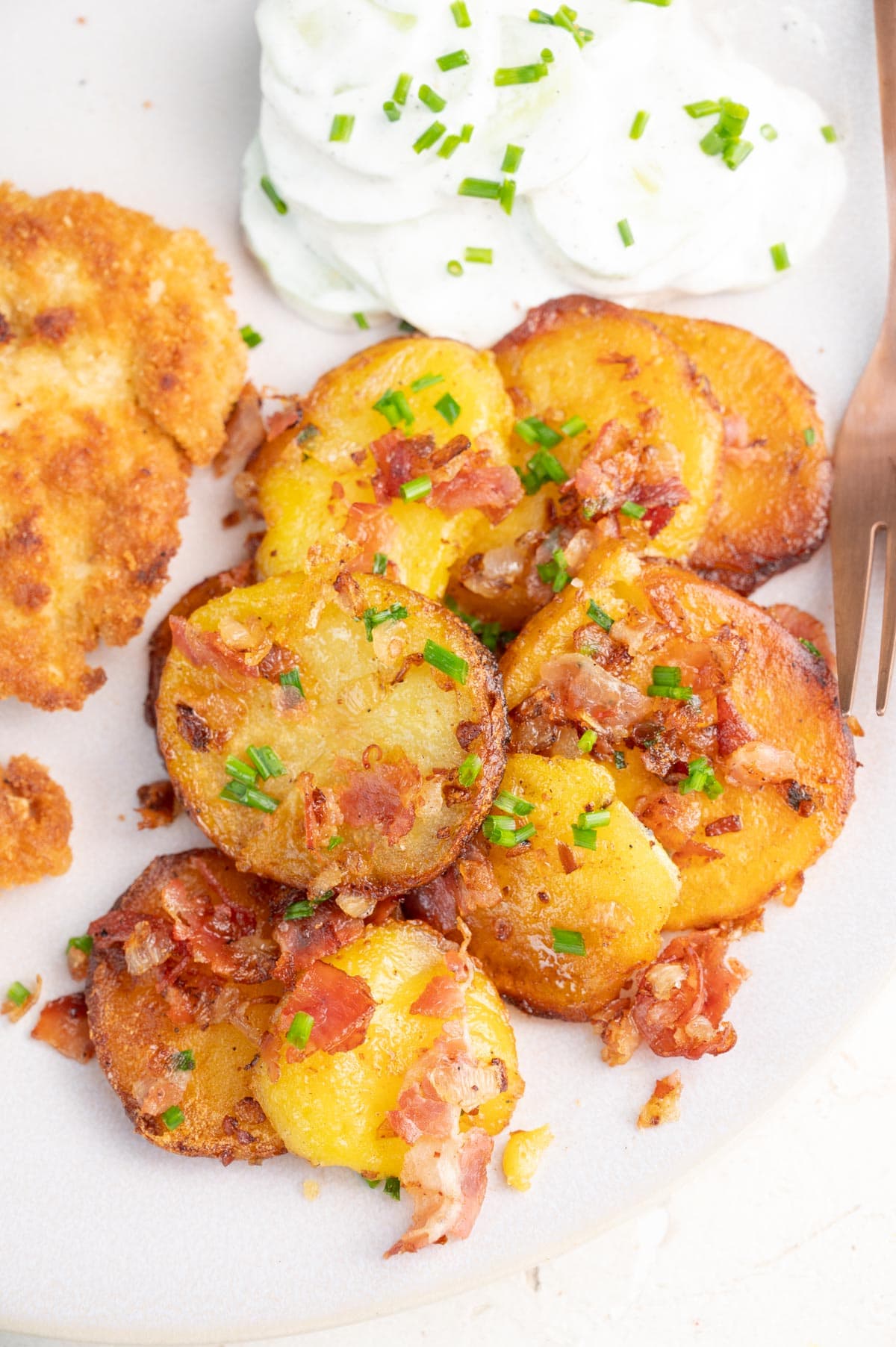 Bratkartoffeln with Schnitzel and cucumber salad on a plate.