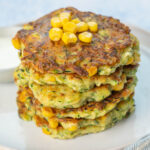 A stack of zucchini corn fritters on a white plate.