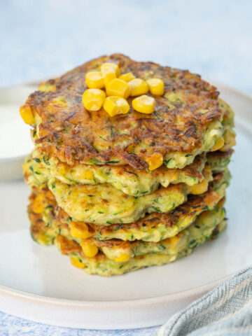 A stack of zucchini corn fritters on a white plate.