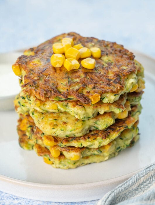 A stack of zucchini corn fritters on a white plate.