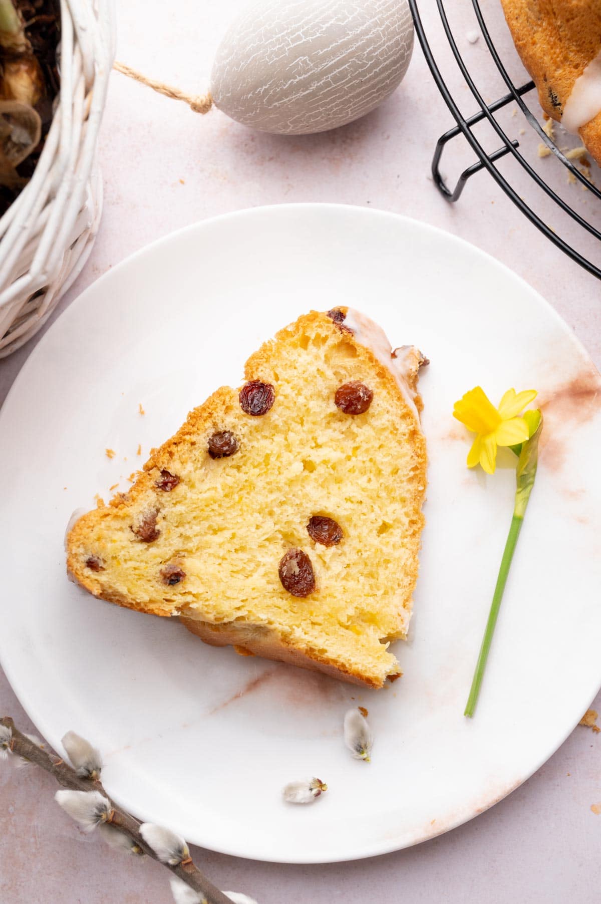 A slice of raisin babka on a white plate surrounded with Easter decorations.