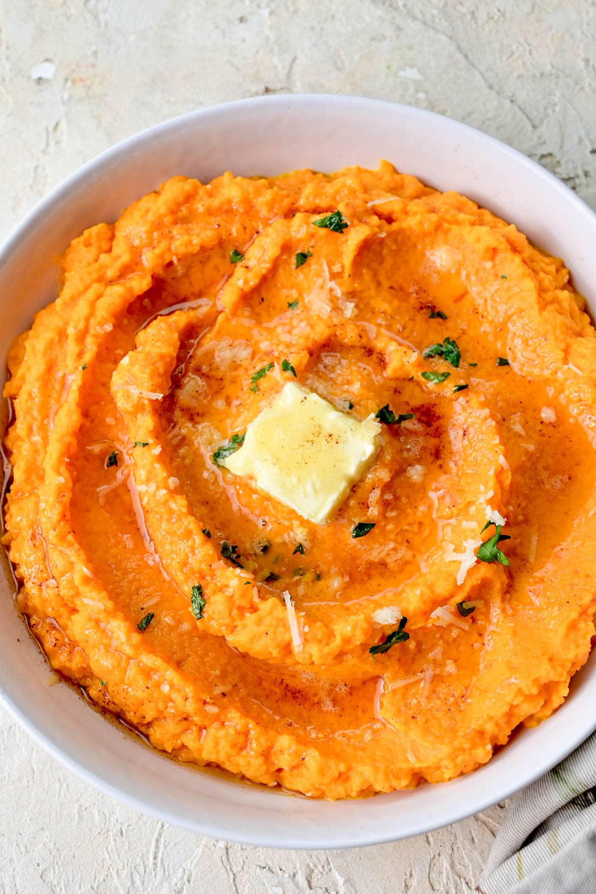 Mashed carrots in a white bowl. topped with butter and parsley.