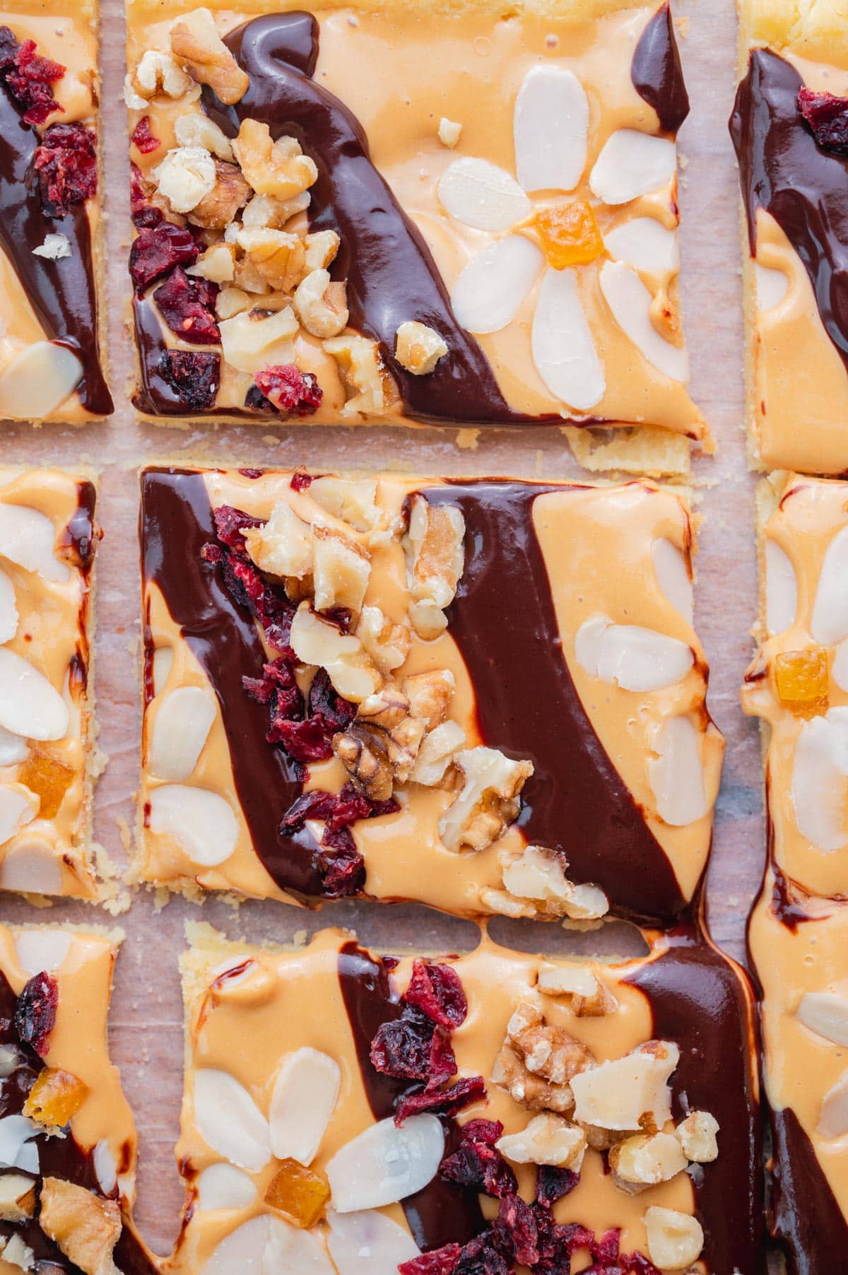 Mazurek kajmakowy topped with chocolate ganache, dried fruit and nuts cut into squares.