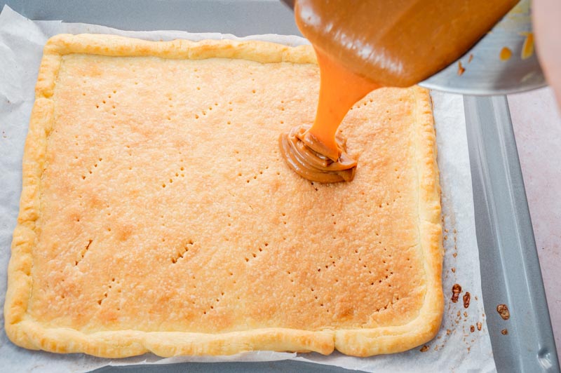 Dulce de leche cream is being poured onto a baked pastry crust.