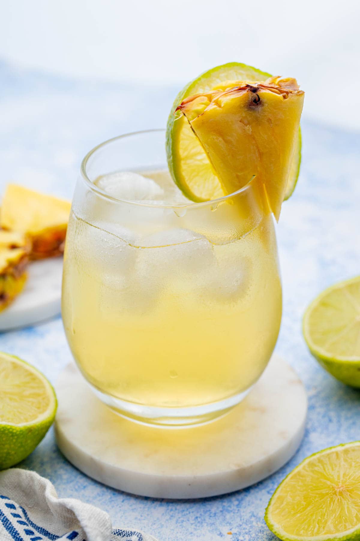 Pineapple vodka drink in a glass garnished with a pineapple wedge and a lime slice.
