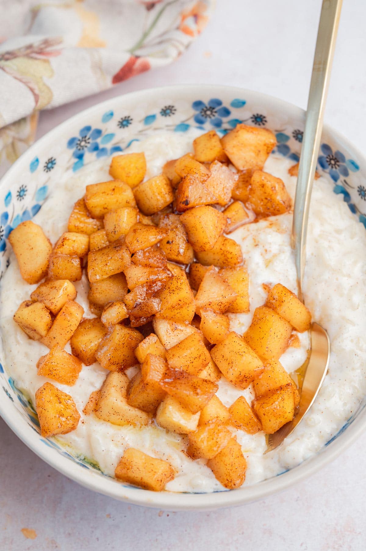 Milchreis in a white bowl topped with  sauteed cinnamon apples.