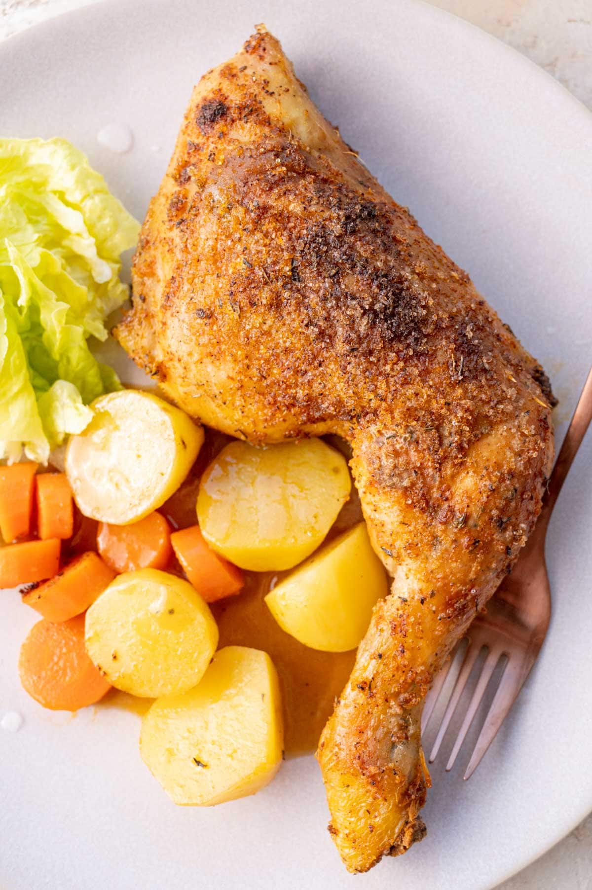 Baked chicken leg with potatoes, carrots, and gravy on a beige plate.