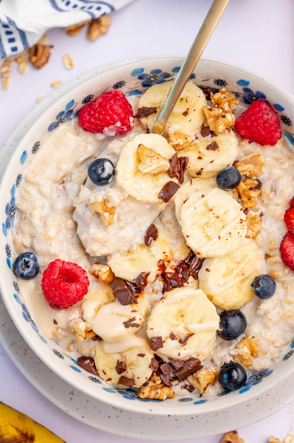 An overhead photo of banana oatmeal topped with sliced bananas, blueberries, and raspberries in a white bowl.