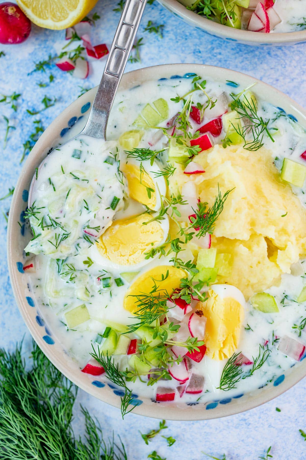 Chlodnik ogorkowy soup in a white bowl topped with eggs, mashed potatoes, radishes, and dill.