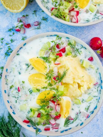 Chlodnik ogorkowy soup in a white bowl topped with eggs, potatoes, and radishes.