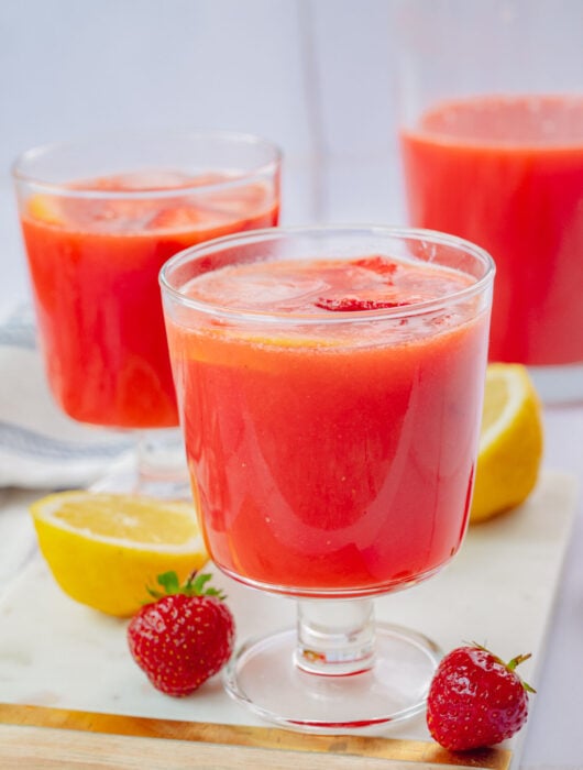 Two glasses with strawberry lemonade on a marble board.