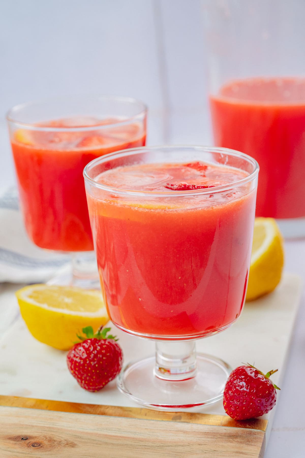 Two glasses with strawberry lemonade. Strawberries and lemons in the background.