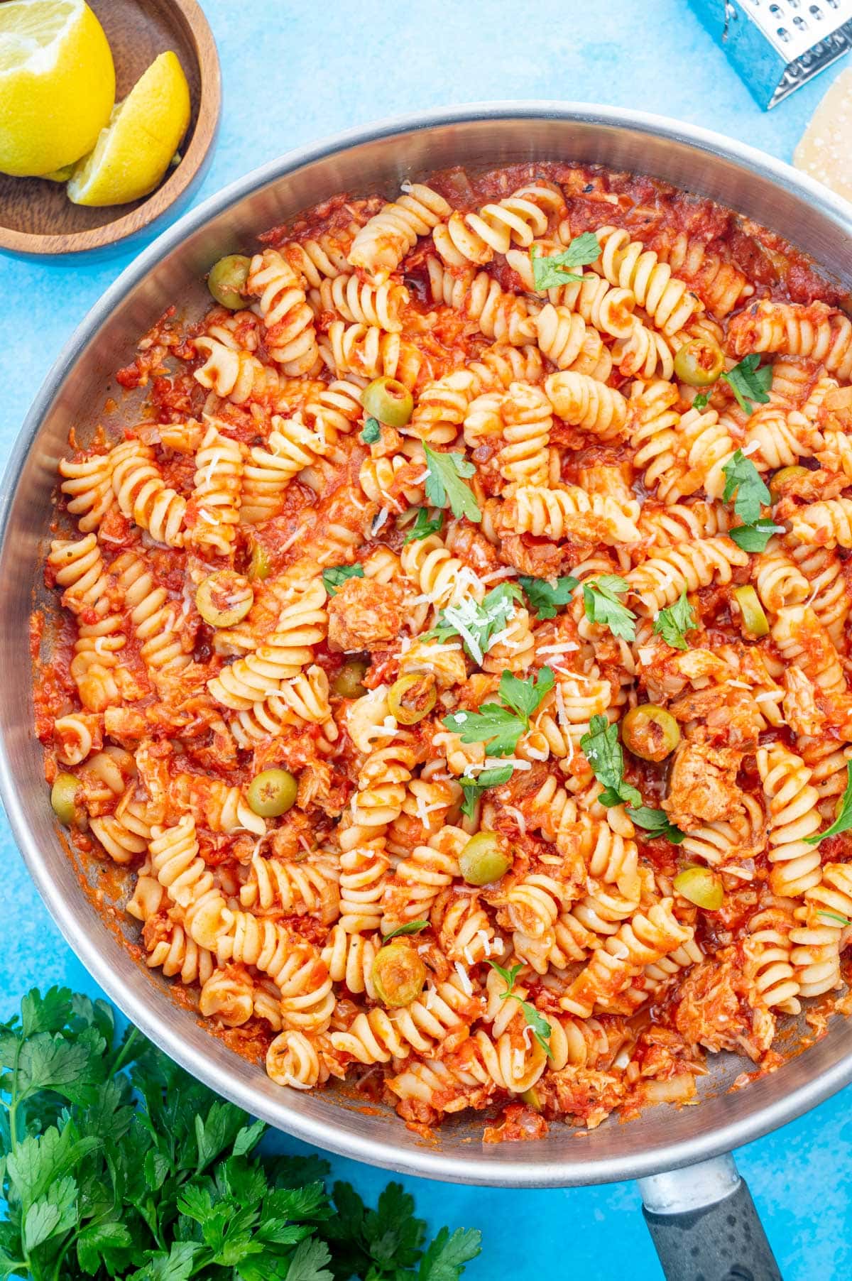 Tuna pasta with tomatoes and olives in a large frying pan on a blue background.