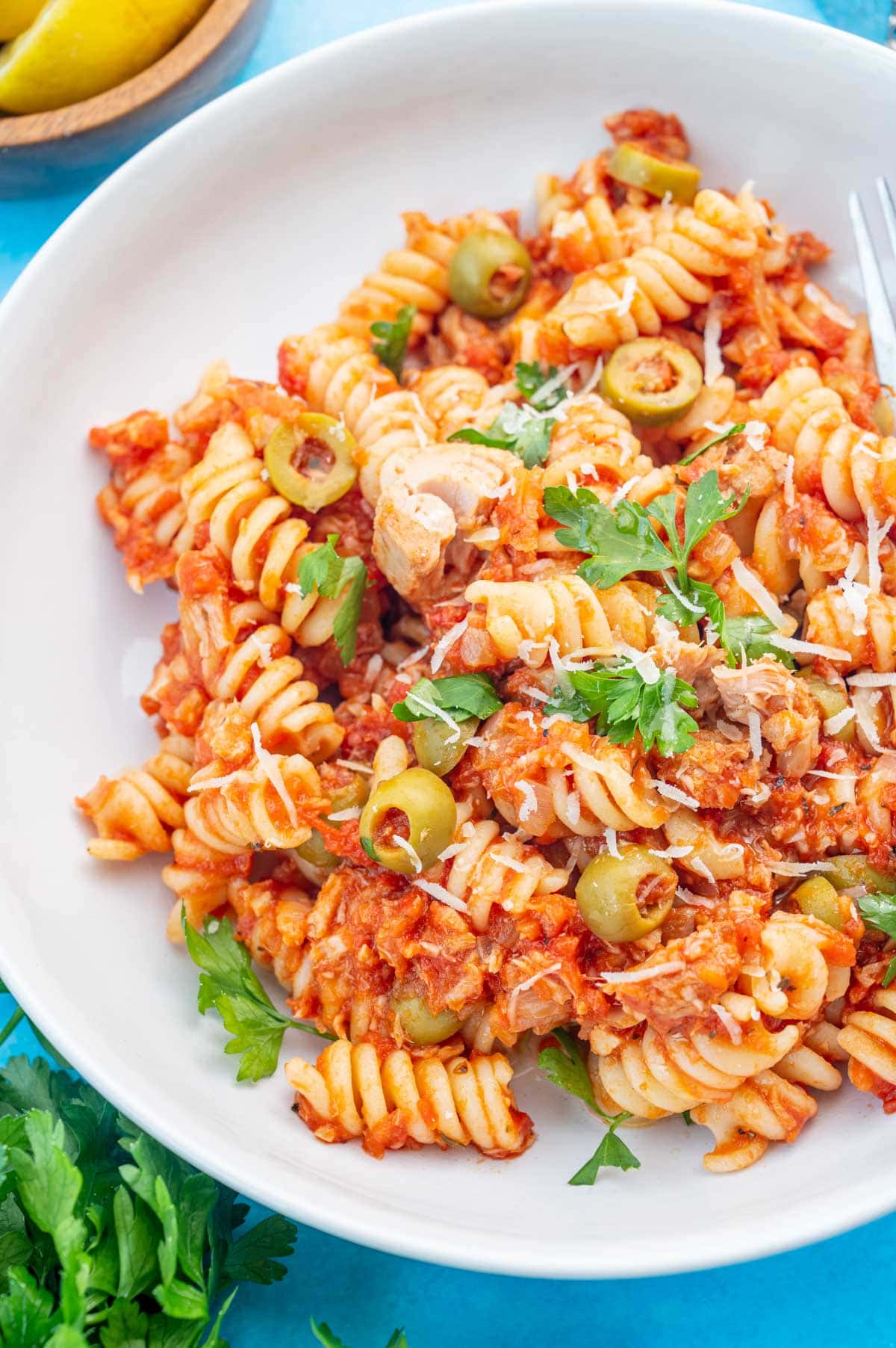 Tuna pasta with olives and tomatoes in a white plate on a blue background.