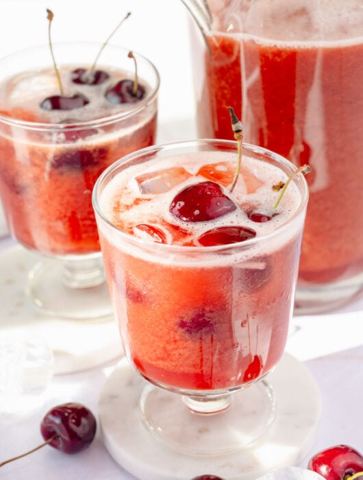 Two glasses and a pitcher with cherry lemonade.