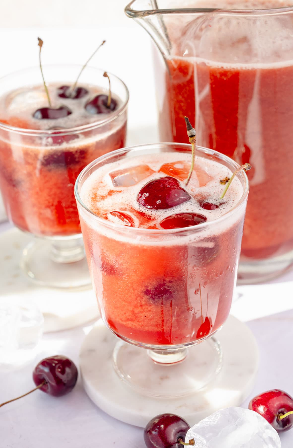 Two glasses and a pitcher with cherry lemonade.